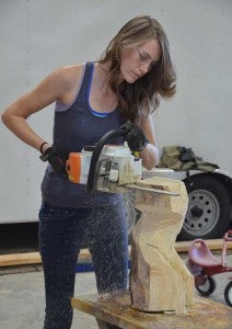 Heather uses a chainsaw to begin a wood sculpture.
