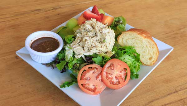 The chicken salad plate is served on a bed of lettuce with fruit and a croissant. 