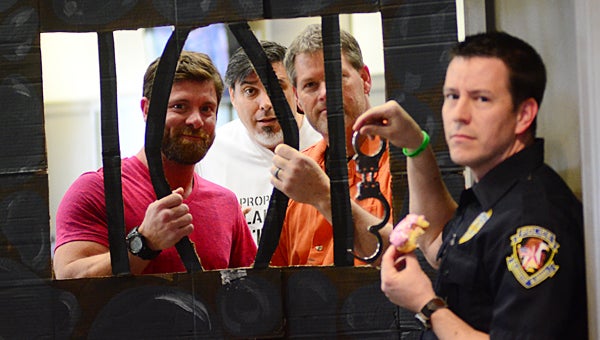 From left, Noah Galloway, Gene Rowley and Brian Copes spend time in a fake jail cell during a March 11 fundraiser at Alabaster City Hall while officer Nathanial Parker, right, supervises them. (Reporter Photo/Neal Wagner)