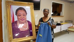 Project leader Cora Dates displays a handmade dress and stands next to a portrait of Shirley Middleton, the inspiration behind the project. (Reporter Photo/Molly Davidson)