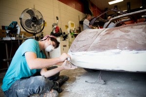 Thompson High School junior Stephen Fuller works on sanding the bumper of an old car being rebuilt into an electric vehicle. (Reporter photo/Keith McCoy)