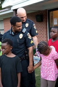 Corporal Charles Brewer (front) and Sergeant Chad Wooten stand hand-in-hand with kids from Kids First Awareness Community Center in Alabaster on a night of prayer for the community. (Reporter Photo/Keith McCoy)