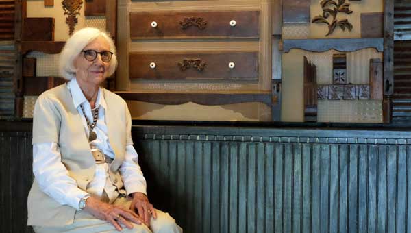 Fay Hutto Black sits in front “Chest of Drawers, Remembered” a composition that includes the remains collected by her in-laws when their beach home was demolished in 1966 by Hurricane Camille. 