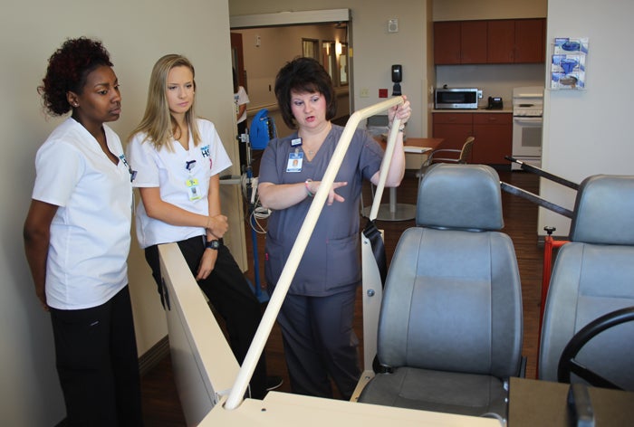 Physical therapist Angel Baker, right, shows students Frederykah Jackson, left, and Olivia Nonnengard a simulator that patients use to practice entering and exiting a vehicle.
